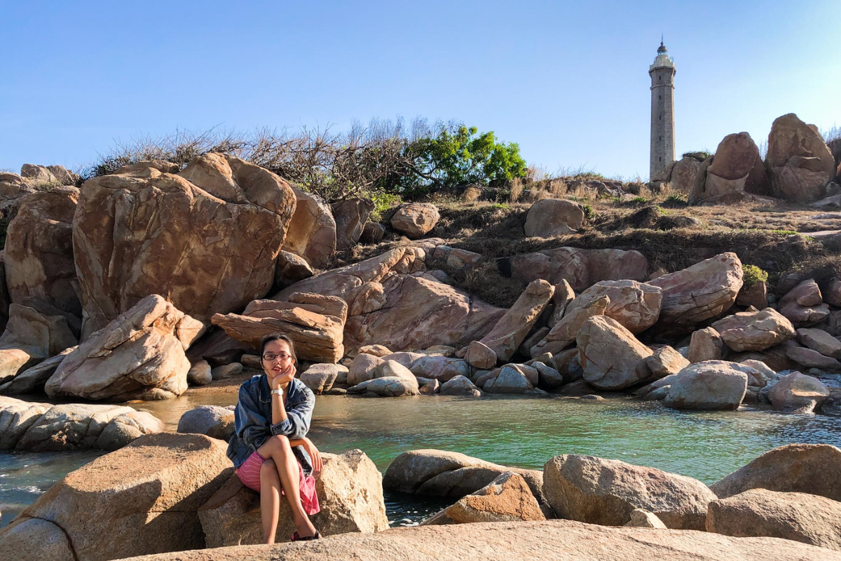 Tourist photographing Ke Ga Lighthouse from rocky cliffs with waves in the background